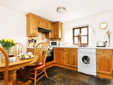 A kitchen with wooden cabinets a dining table chairs and a washing machine at The Shippon Near Launceston