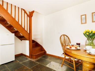 A wooden staircase next to a white refrigerator and a wooden table with chairs and a plate of scones at The Shippon Near Launceston