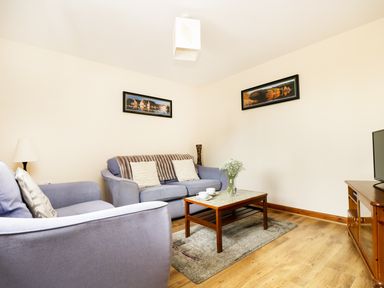 A living room with two sofas a coffee table with cups and flowers a TV on a wooden stand and landscape pictures on the wall at The Shippon Near Launceston