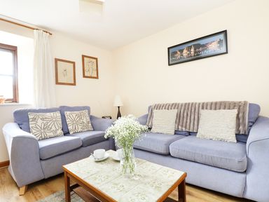 A living room with two blue sofas a coffee table with a vase of flowers and framed pictures on the wall at The Shippon Near Launceston