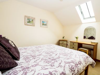 A bedroom with a bed chest of drawers a stool and a skylight window at The Shippon Near Launceston