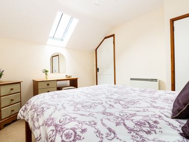 A bedroom with a bed covered with a patterned duvet a dresser with a mirror and flowers by a skylight window at The Shippon Near Launceston