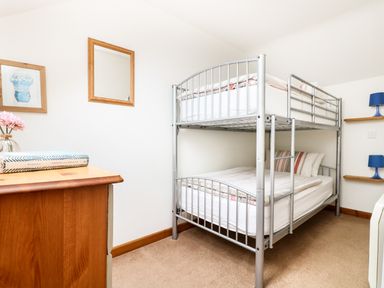 A bedroom with a metal bunk bed a wooden chest of drawers and framed pictures on the wall at The Shippon Near Launceston