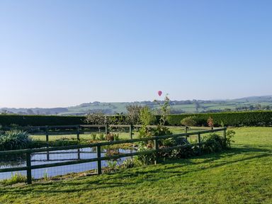 A garden with a pond enclosed by wooden fencing and hills in the background at The Wagon House in Polyphant near Launceston