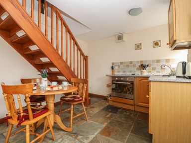 A kitchen with wooden table and chairs under a wooden staircase at The Wagon House in Polyphant near Launceston