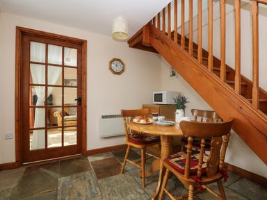 A dining area with wooden table and chairs under a staircase and a glass door with curtains at The Wagon House in Polyphant near Launceston