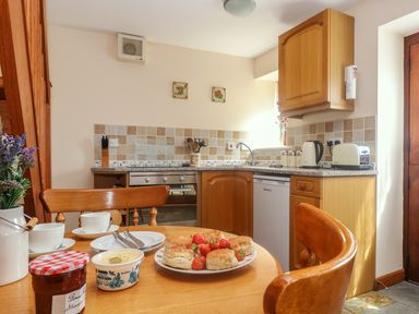 A kitchen with wooden cabinets a small refrigerator a toaster a kettle and a table with scones strawberries jam and cream at The Wagon House in Polyphant near Launceston