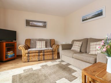 A living room with two sofas a television on a wooden cabinet and a small wooden table with flowers at The Wagon House in Polyphant near Launceston