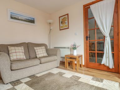 A living room with a sofa two cushions a floor lamp and a side table with flowers at The Wagon House in Polyphant near Launceston