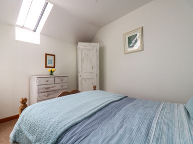 A bedroom with a bed covered in blue blankets a chest of drawers with yellow flowers and a wardrobe under a skylight at The Wagon House in Polyphant near Launceston