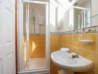 A bathroom with a shower cubicle and a sink with a mirror above at The Wagon House in Polyphant near Launceston