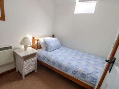 A small bedroom with a single bed with blue and white checked bedding a wooden nightstand with a lamp and a skylight window at The Wagon House in Polyphant near Launceston