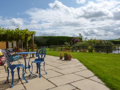 A patio with blue metal chairs and table next to a garden with plants and a pond at The Wagon House in Polyphant near Launceston