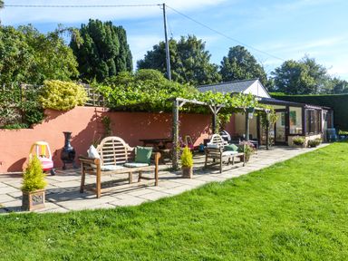A garden patio with wooden benches and grapevine-covered pergola at The Wagon House in Polyphant near Launceston