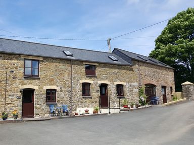 A stone building with multiple doors and windows and outdoor chairs and flower pots at The Wagon House in Polyphant near Launceston