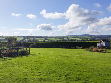 A large grassy field with a wooden fence small garden and a playhouse with a slide at The Wagon House in Polyphant near Launceston