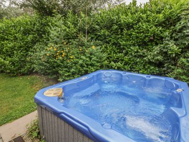 A blue hot tub bubbling in a garden with green bushes and yellow flowers at Langdale Lodge 15 White Cross Bay near Troutbeck Bridge