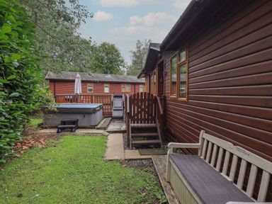 A garden area with a wooden bench a hot tub and two wooden lodges at Langdale Lodge 15 White Cross Bay near Troutbeck Bridge