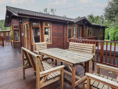 An outdoor wooden deck with wooden table and benches in front of a wooden cabin at Langdale Lodge 15 White Cross Bay near Troutbeck Bridge
