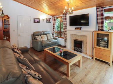 A living room with leather sofas a coffee table a fireplace a mounted TV and a wooden cabinet at Langdale Lodge 15 White Cross Bay near Troutbeck Bridge