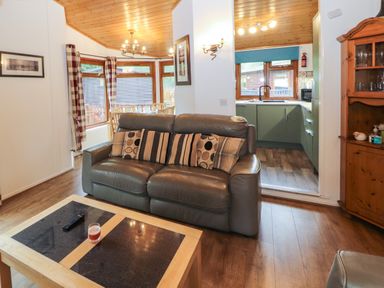 A living room with a gray leather sofa and patterned cushions next to a wooden coffee table with a candle and remote control at Langdale Lodge 15 White Cross Bay near Troutbeck Bridge