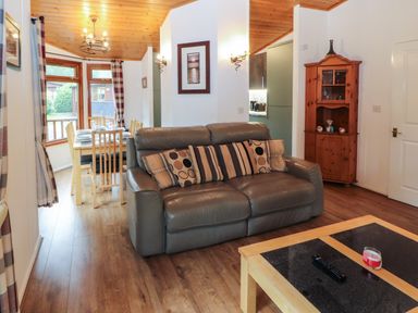 A living room with a leather sofa wooden dining table chairs a corner cabinet and a coffee table at Langdale Lodge 15 White Cross Bay near Troutbeck Bridge