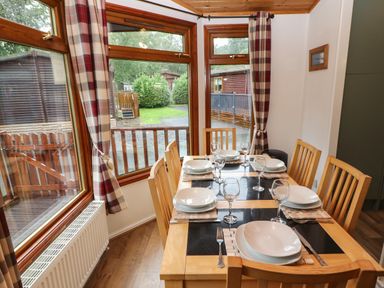 A dining area with a wooden table set for six near windows with plaid curtains at Langdale Lodge 15 White Cross Bay near Troutbeck Bridge