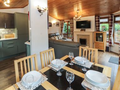 A dining area with a set table next to a living room with sofas a television and a fireplace at Langdale Lodge 15 White Cross Bay near Troutbeck Bridge