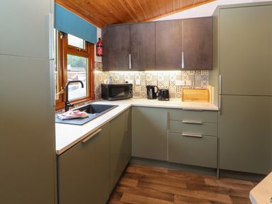 A kitchen with green and grey cabinets a black sink an oven microwave toaster kettle and window at Langdale Lodge 15 White Cross Bay near Troutbeck Bridge