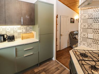 A kitchen area with green cabinets a bread box a kettle a toaster and a gas stove next to a living room with a sofa at Langdale Lodge 15 White Cross Bay near Troutbeck Bridge
