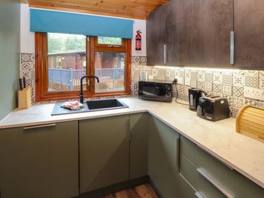 A kitchen with a window above a sink a microwave kettle toaster and knife block on the counter at Langdale Lodge 15 White Cross Bay near Troutbeck Bridge