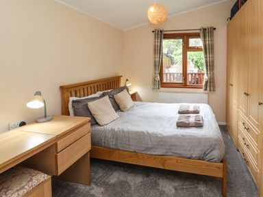 A bedroom with a wooden bed and side tables a desk with a lamp and wardrobes by the window at Langdale Lodge 15 White Cross Bay near Troutbeck Bridge