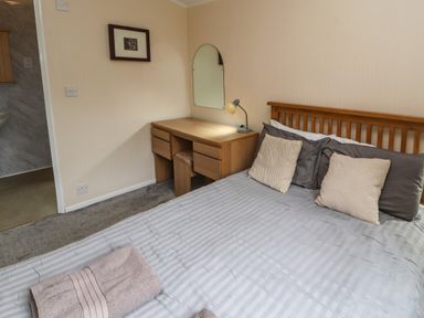 A bedroom with a wooden bed, pillows, folded towels, a desk with a lamp, and a mirror on the wall at Langdale Lodge 15 White Cross Bay near Troutbeck Bridge