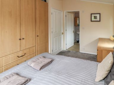 A bedroom with a bed with folded towels a wooden wardrobe a desk and an open door leading to a bathroom at Langdale Lodge 15 White Cross Bay near Troutbeck Bridge