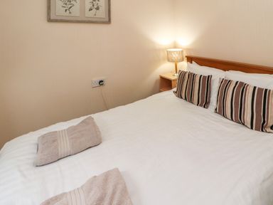A bedroom with a bed with striped pillows and folded towels on white bedding at Langdale Lodge 15 White Cross Bay near Troutbeck Bridge