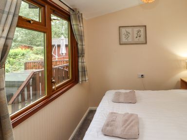 A bedroom with a bed and towels on it next to a window with plaid curtains and a framed picture on the wall at Langdale Lodge 15 White Cross Bay near Troutbeck Bridge