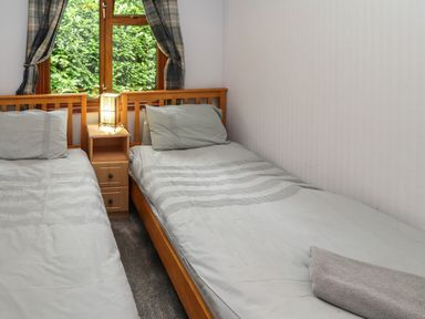 A bedroom with two single beds a wooden bedside table and a window with curtains at Langdale Lodge 15 White Cross Bay near Troutbeck Bridge