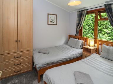 A bedroom with two single beds a wooden wardrobe a bedside table with a lamp and a window with plaid curtains at Langdale Lodge 15 White Cross Bay near Troutbeck Bridge