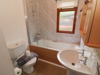 A bathroom with a toilet, a bathtub with a shower, a sink, and a window with a blind at Langdale Lodge 15 White Cross Bay near Troutbeck Bridge