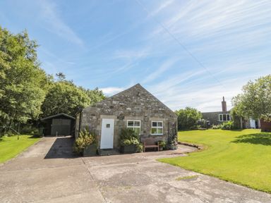 A stone building with two windows and a door a bench and plants outside a green shed driveway and lawn at Drovers Rest in Otterburn