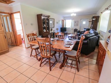 A dining area with a wooden table set for four and a living room with black leather sofas at Drovers Rest in Otterburn