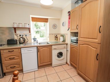 A kitchen with wooden cabinets a dishwasher a washing machine and a window at Drovers Rest Otterburn