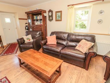 A living room with leather sofa and armchair a wooden coffee table bookshelf and a wall clock at Drovers Rest in Otterburn