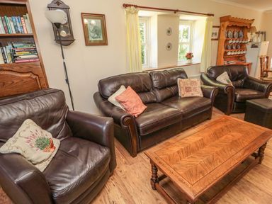 A living room with leather sofas wooden coffee table bookshelf and window with yellow curtains at Drovers Rest in Otterburn