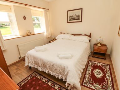 A bedroom with a double bed white bedding two small rugs wooden nightstands lamps and two windows at Drovers Rest Otterburn
