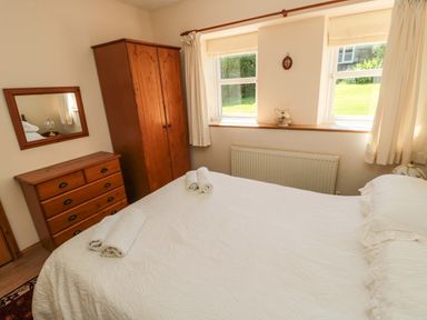 A bedroom with a bed with white bedding two rolled towels on the bed a wooden wardrobe and a wooden chest of drawers with a mirror above at Drovers Rest Otterburn