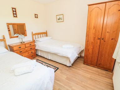 A bedroom with two single beds a wooden wardrobe and a dresser with a mirror and lamp at Drovers Rest in Otterburn