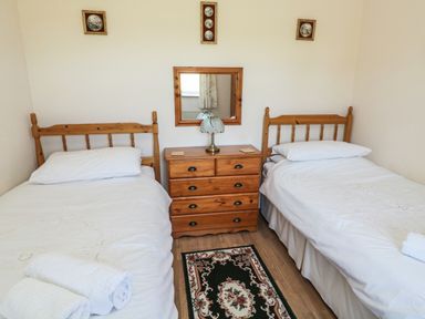 A bedroom with two single wooden beds a wooden dresser with a lamp and a mirror above and a rug on the floor at Drovers Rest Otterburn