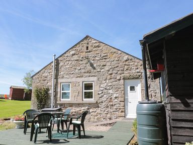 A backyard patio with plastic chairs and table beside a stone building and green water barrel at Drovers Rest Otterburn