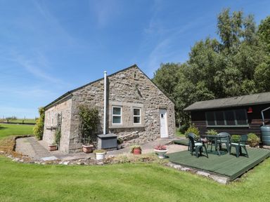 A stone cottage with a garden patio set on a wooden deck next to a wooden shed at Drovers Rest in Otterburn